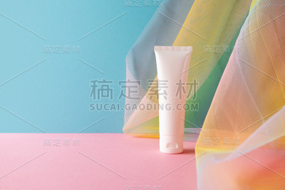 白色塑料管的美容产品在蓝色粉红色的背景与彩色彩虹透明纱渔网织物窗帘