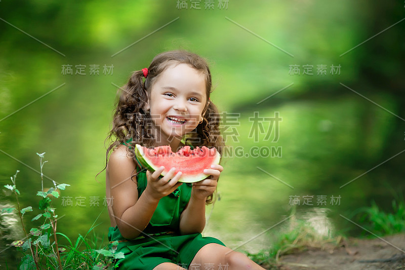 可爱的女孩坐在河边，吃着一片新鲜的红西瓜