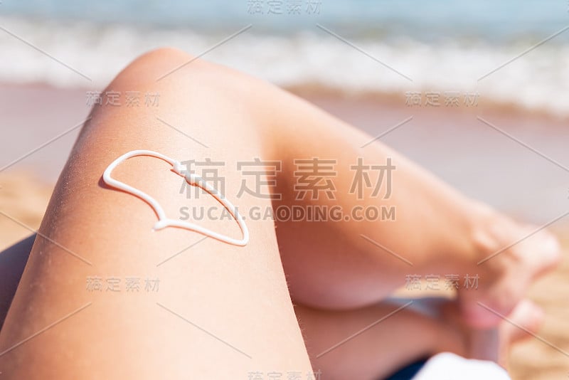 涂在女人腿上心脏形状的防晒霜，在海边浴巾上晒太阳