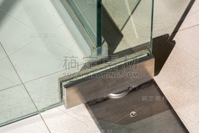 玻璃门配件，旋转机构将门的金属环固定在地砖上闭合。