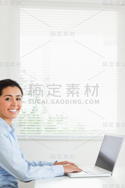 美丽的女人工作与她的笔记本电脑和摆姿势而坐