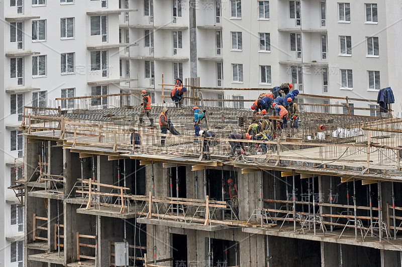 在已建建筑物的背景上建造一座新房子。许多戴着头盔和面具的建筑工人又掀了一层楼