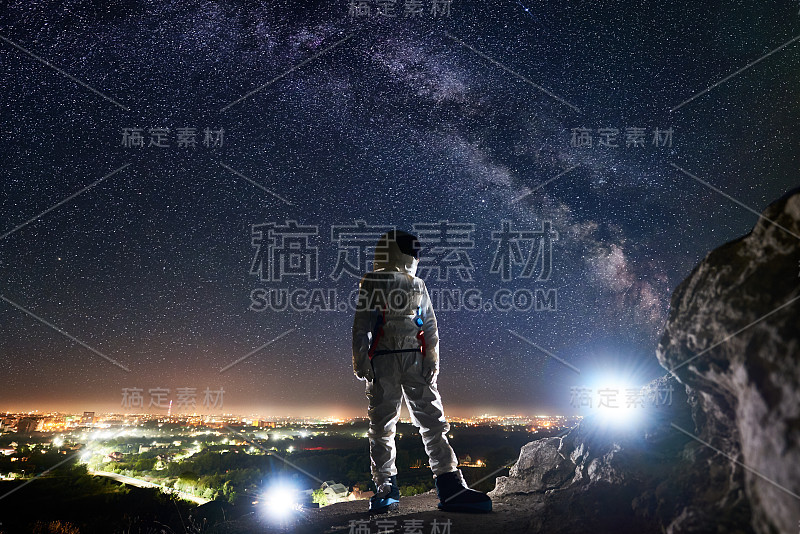 宇航员站在布满星星的夜空下的岩石山上。