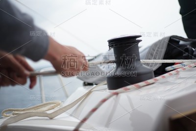 一个人的双手正在卷一根绳子，帆船上的升降索缠绕着绞车