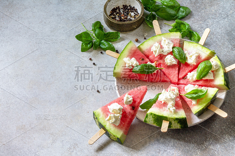 健康的季节性饮食和营养，夏日小吃。灰色的石头桌上放着西瓜披萨、羊乳酪和罗勒。副本的空间。