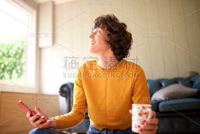 微笑的女人坐在家里，喝着酒，手机看着别处