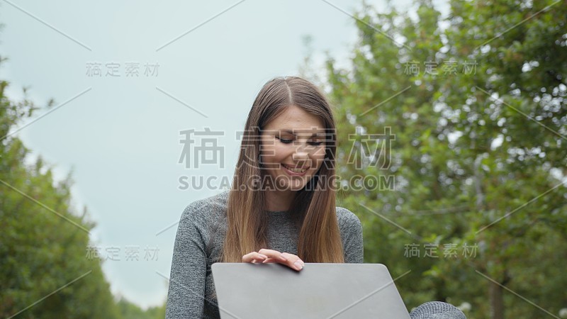 女人打开笔记本电脑，开始在键盘上打字，树木在大自然中。女性从事商业或自由职业，在大自然或新鲜空气在惊