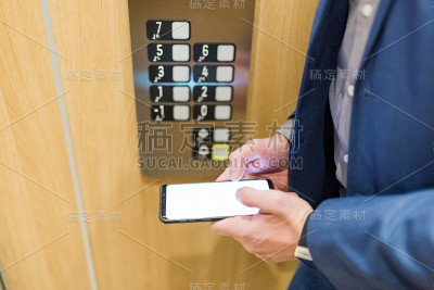 西装男在商务办公楼的电梯里使用黑屏手机。