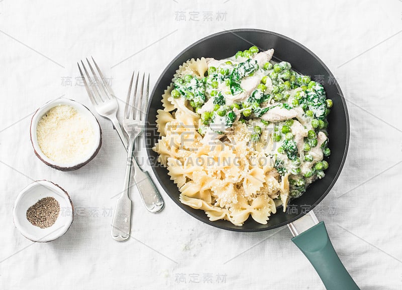 一锅奶油鸡肉菠菜和绿色豌豆farfalle意大利面在白色的背景，俯视图。平躺