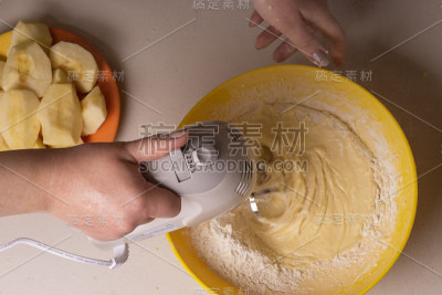 一位妇女在一个黄色的碗里用电动搅拌机搅拌馅饼的原料。