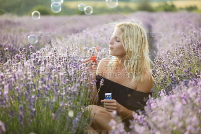 可爱的金发女人在日落吹肥皂泡。