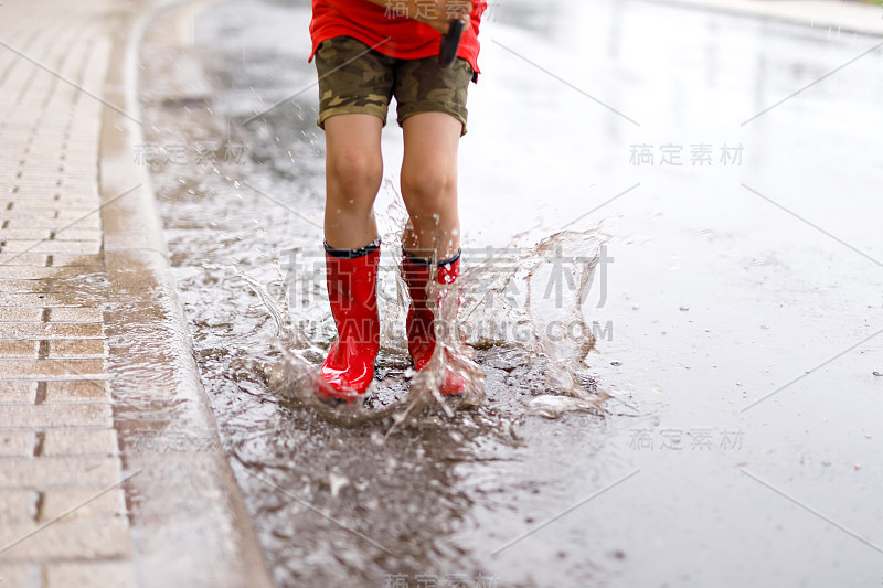 孩子穿着红雨靴跳进水坑里。