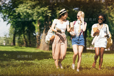 开朗迷人的多民族女孩戴着太阳镜，拿着课本在公园里散步