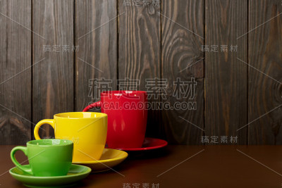 不同大小和颜色的陶瓷杯咖啡和茶-红色，黄色和绿色在黑暗的木制背景。