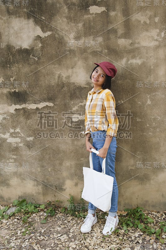 快乐的年轻亚洲女孩携带布袋与棕色的背景。