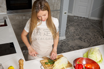 一个年轻的金发女人正在家庭厨房里用刀切菜。