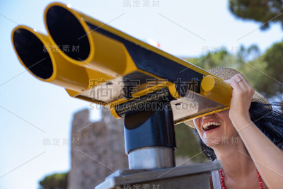 一位女游客用双筒望远镜观看城市景观。