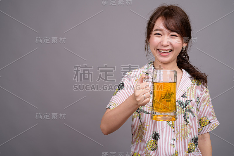 工作室拍摄的年轻美丽的亚洲女人拿着一杯啤酒在灰色的背景