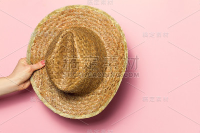 年轻女子的手拿着粉红色背景上的夏季草帽。