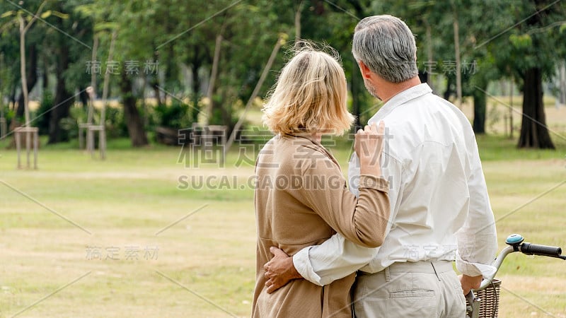 背后幸福浪漫的老两口拥抱在一起，老婆婆手搭在男人的肩膀上，丈夫搂住妻子的腰，退休后的生活方式周末在公