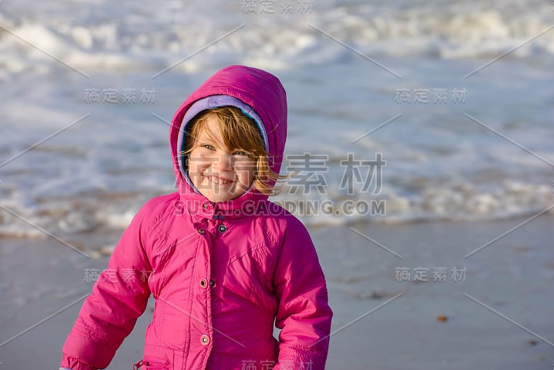 一个穿着连帽夹克的小女孩在寒冷的海滩上玩耍