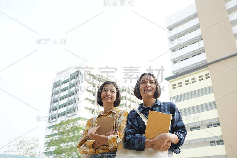 两个快乐的年轻亚洲女孩携带布袋和笔记本在大学。