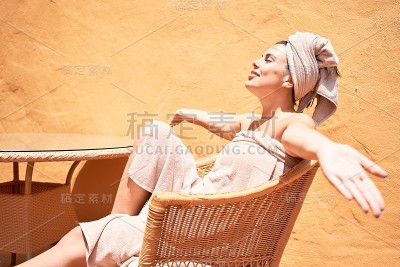 年轻漂亮的女人穿着浴巾坐在椅子上在阳台上晒太阳
