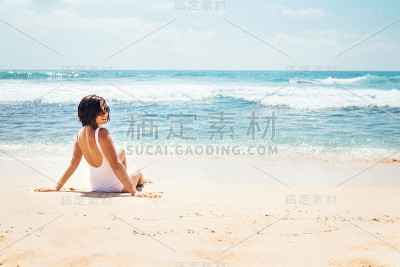 在阳光明媚的日子里，穿着白色泳衣的女人坐在空旷的海滩上