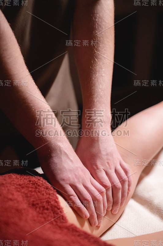 男士优质豪华臀部按摩减肥健康中心。一个男性按摩师做腿部按摩的女性客户在一个办公室与黑暗的光