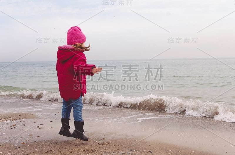 穿着红夹克的小女孩在海滩上玩海浪