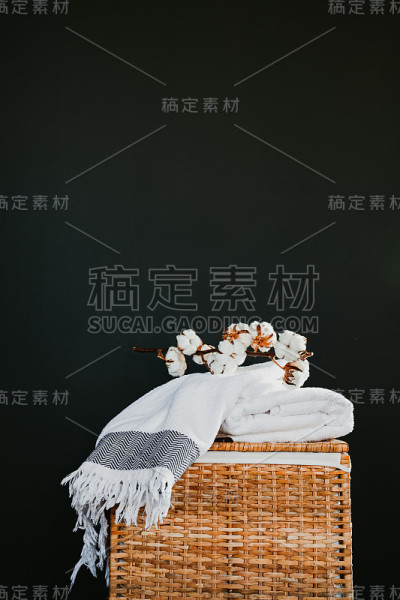 在洗衣房黑色的墙壁上，白色的棉质毛巾放在有棉枝的藤盒上。