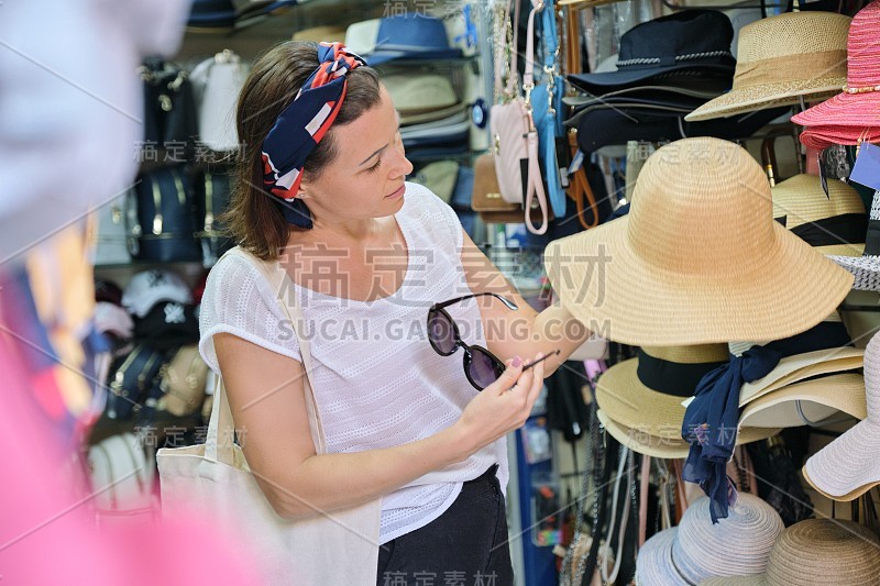 一个成熟的女人在街上的商店买太阳帽