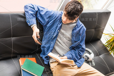 在家里或公寓里有手机和书的年轻男孩