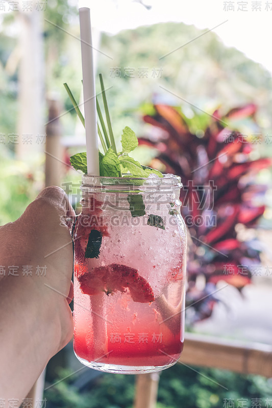 男人手里拿着一杯草莓汁和苏打水。热带咖啡馆背景。巴厘岛