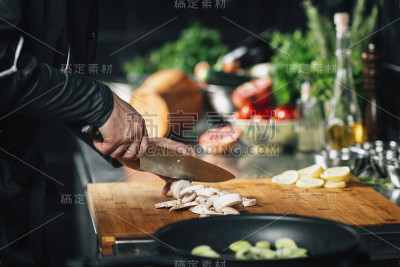 烹饪晚餐-厨师拿着一把刀，在一个木制砧板上切蘑菇