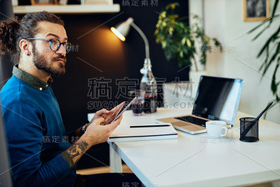 年轻的微笑迷人的白种人胡须平面设计师坐在办公室和使用平板电脑。