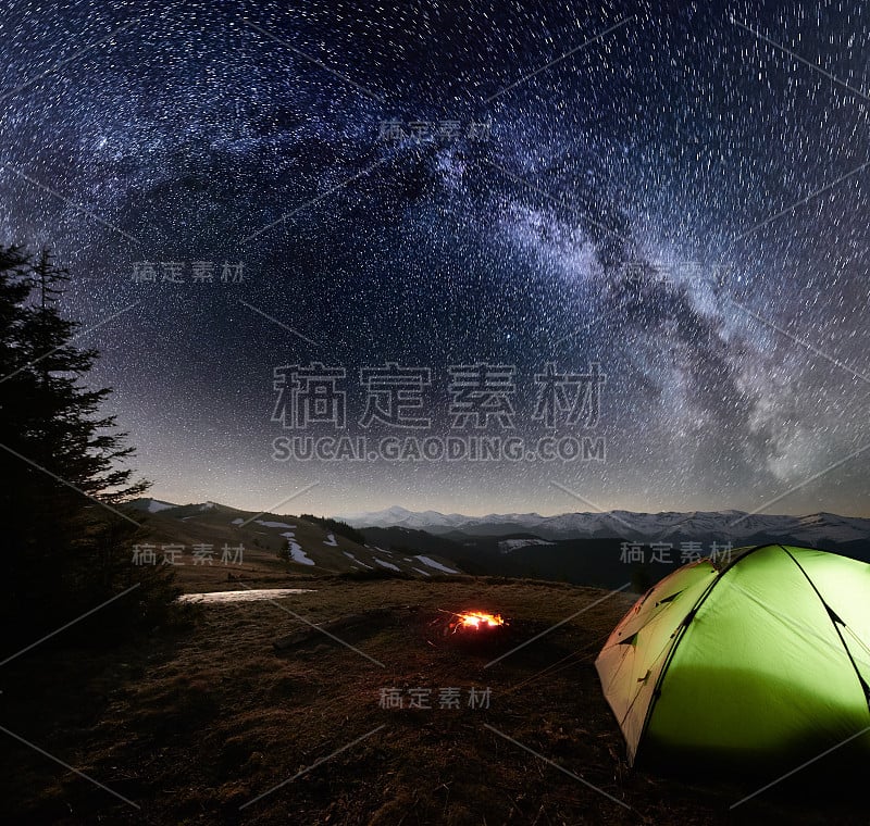 晚上在山里露营。在满是星星和银河的美丽夜空下，明亮的帐篷和篝火