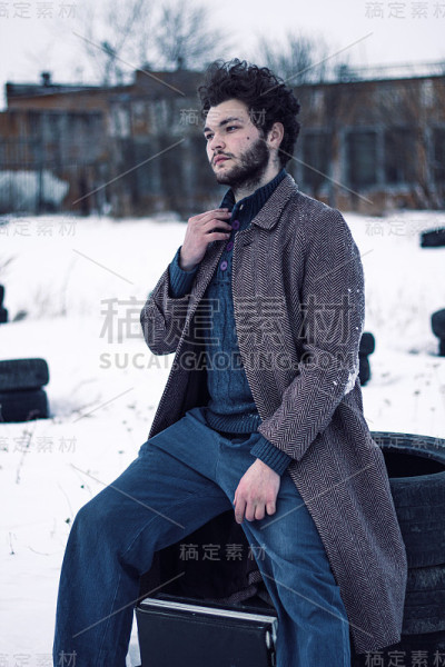 一个穿着苏联外套，蓄着胡须的英俊男子坐在轮胎上