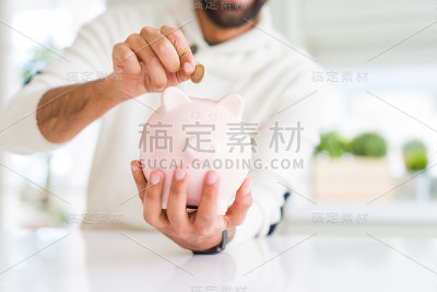 一名男子将一枚硬币放入小猪储蓄罐，为投资储蓄