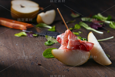 木桌上放着火腿和梨