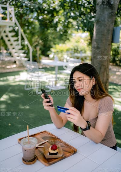 美丽微笑的年轻亚洲女性管理网上银行与手机应用程序在智能手机上，并进行移动支付与信用卡。