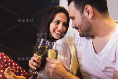 年轻夫妇男女在床上亲密地喝着香槟