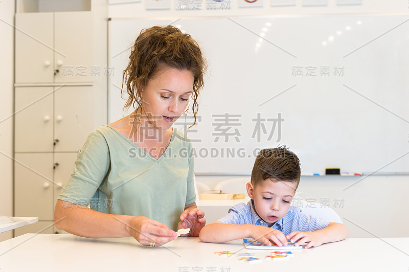 女教师和学龄前的男孩在教室里玩拼图游戏