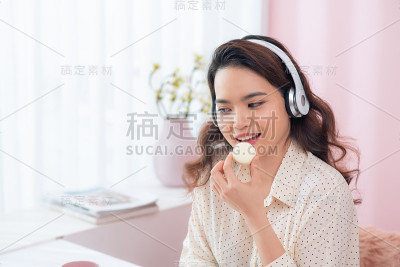 年轻的亚洲女人一边听音乐一边吃马卡龙。
