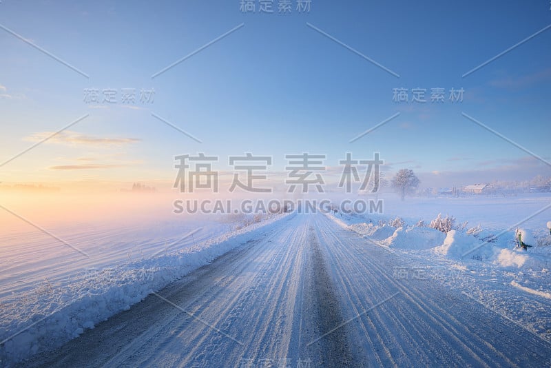 冬季日落时，雾气笼罩着一条被雪覆盖的乡村公路