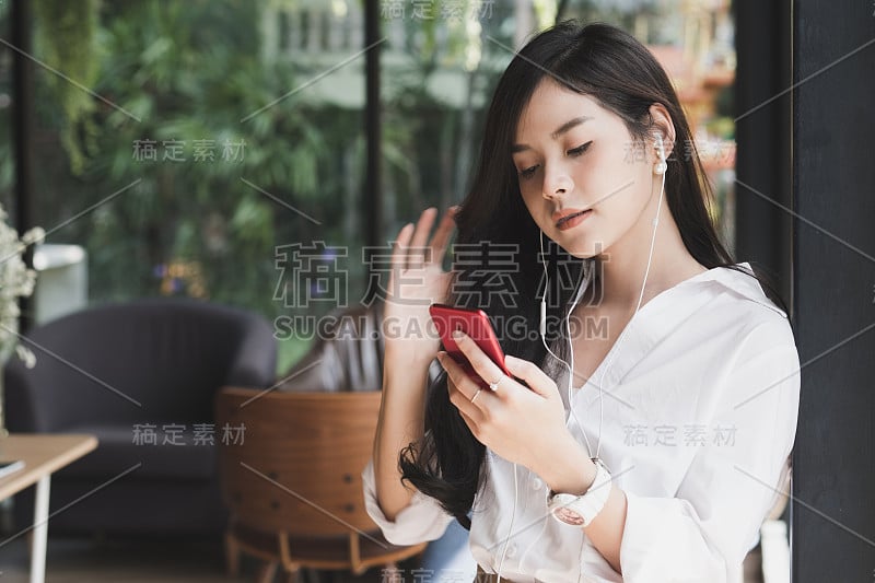 一个女人拿着智能手机在咖啡馆里听着音乐。休闲，生活方式，人的理念