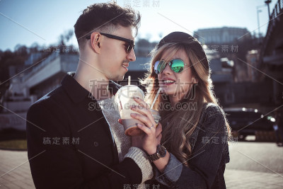 一对可爱的情侣在街上散步，喝着鸡尾酒