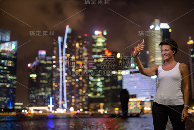在新加坡滨海湾，一个成熟的女人在晚上用手机自拍