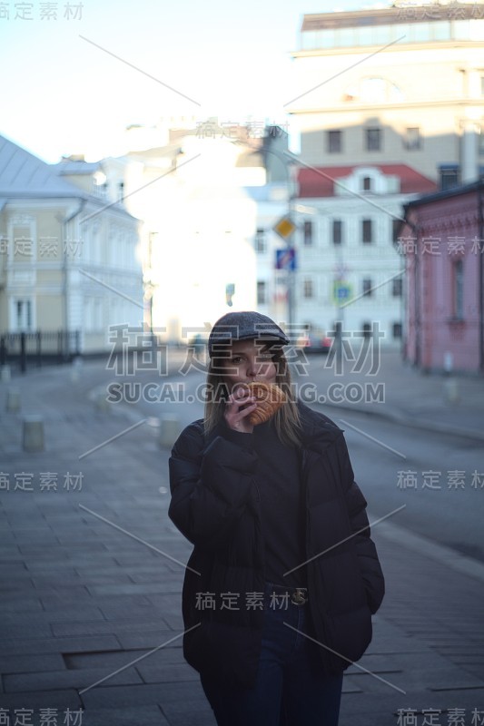 年轻漂亮的女孩在街上吃牛角面包