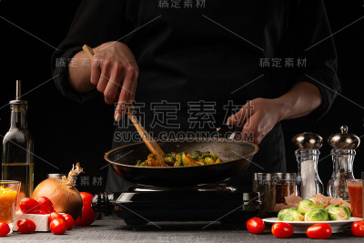 厨师烹饪。用平底锅煎菜。餐厅经营，以黑色为背景，横放照片。食材、咖啡或餐饮业务。
